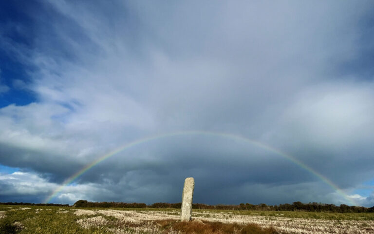 A standing stone in a field in front of a rainbow